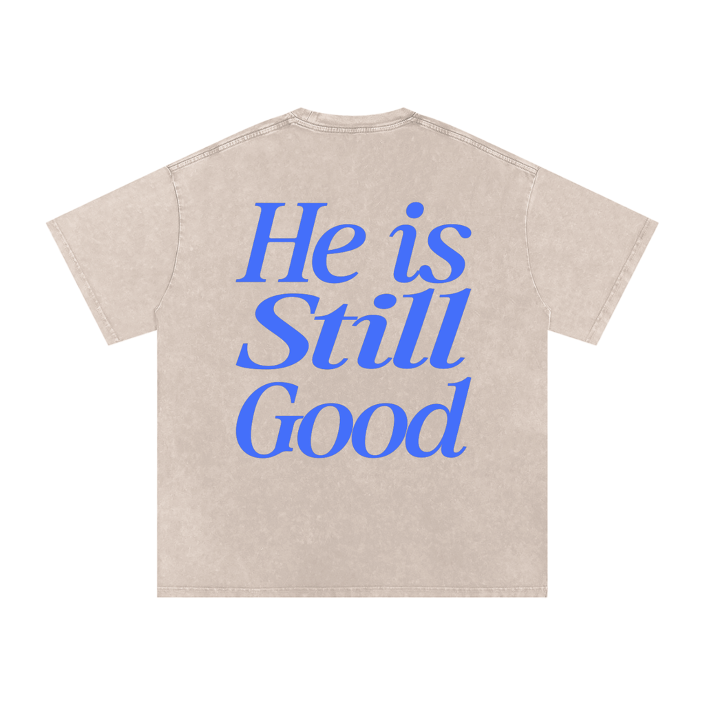 Beige t-shirt with blue text 'He is Still Good' on a white background